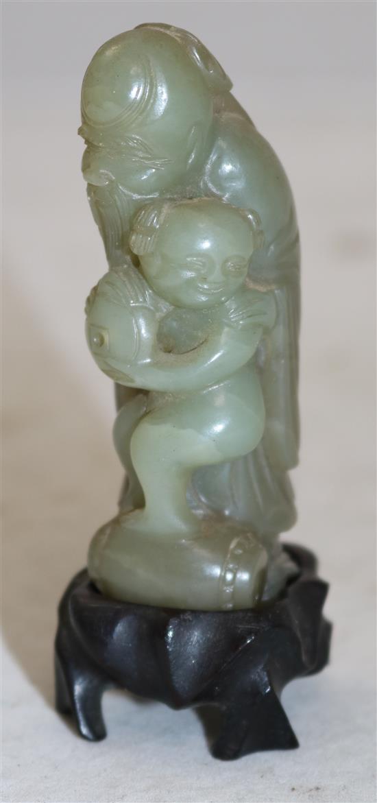 A Chinese celadon and brown jade group of Shou Lao and a boy standing upon a barrel, 18th/19th century, 7.3cm, ebonised wood stand